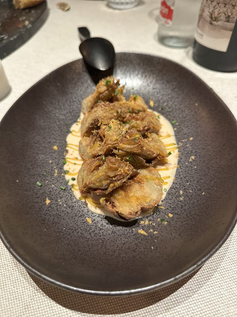 Alcachofas fritas doradas acompañadas de foie gras suave y una yema de huevo curada, mostrando una combinación de texturas y colores vibrantes
