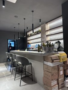 Barra del Serralunga Wine Bar con taburetes grises, iluminación cálida y detalles modernos.