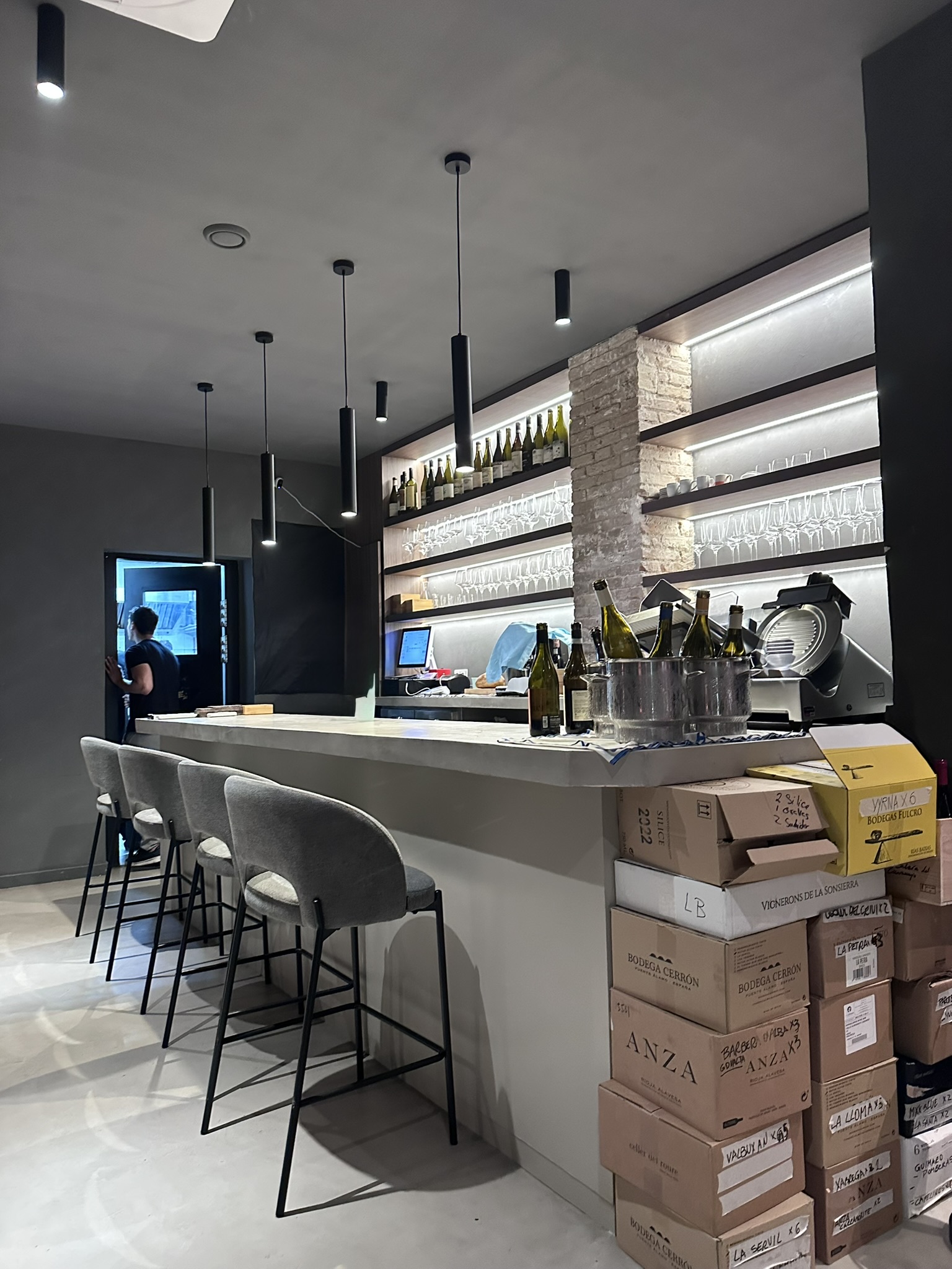 Barra del Serralunga Wine Bar con taburetes grises, iluminación cálida y detalles modernos.