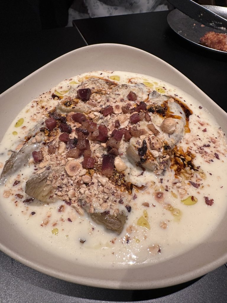 Berenjena asada servida con crema de queso pecorino, salsa macha picante y láminas de guanciale crujiente.