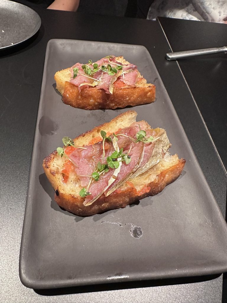 Plato de bonito en semisalazón marcado a la llama, con tomate de penjar, albahaca fresca y base de focaccia tostada.