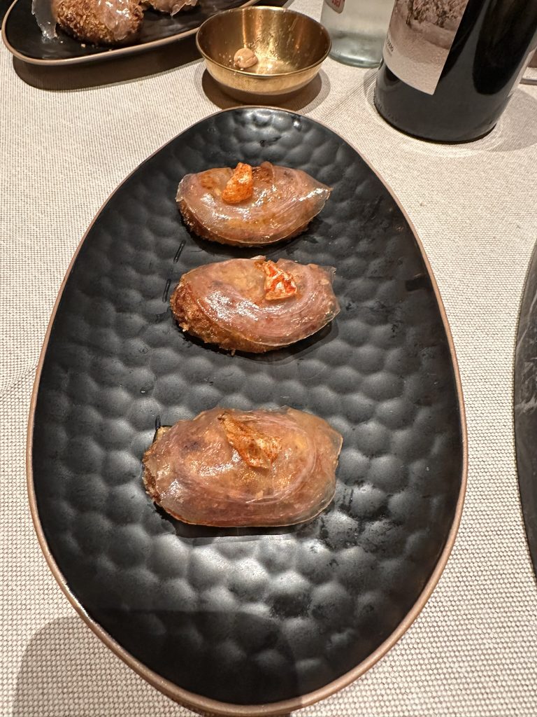 Croqueta dorada y crujiente rellena de torreznos de Soria en bechamel, cubierta con lámina de panceta y airbag de piel de torrezno, mostrando capas y detalles de la preparación