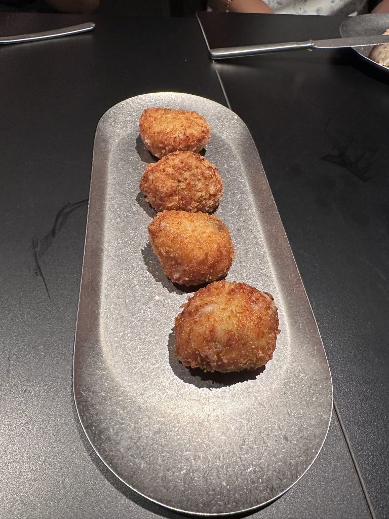 Croqueta crujiente de cecina sobre plato de cerámica, con interior cremoso y dorado perfecto.