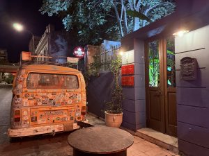 Entrada del restaurante El Cerdo Negro 1985 en Atenas, con varias menciones Michelin visibles en rojo y una furgoneta estilo surf aparcada en la puerta