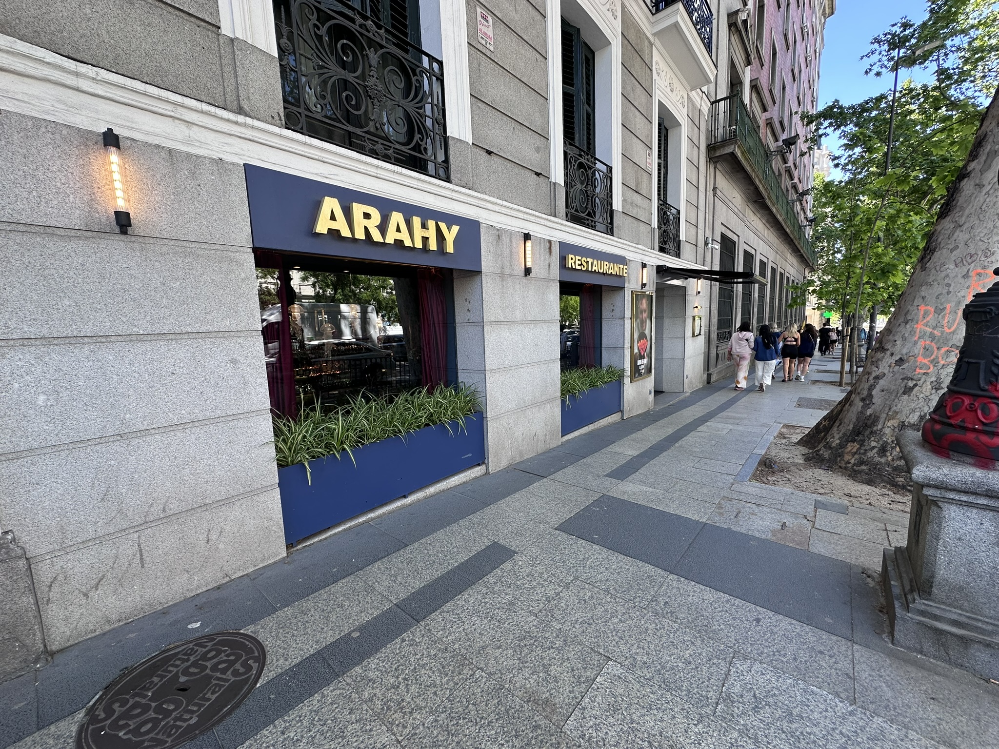 Fachada del restaurante Arahy en Madrid con su cartel dorado sobre fondo azul, junto a la Puerta de Alcalá