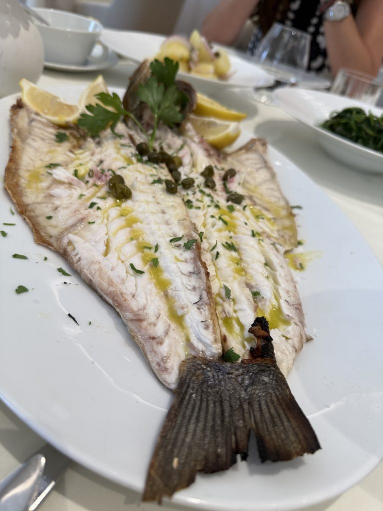 Lubina entera a la parrilla servida en Milos Restaurant, con piel crujiente y acompañamiento de limón