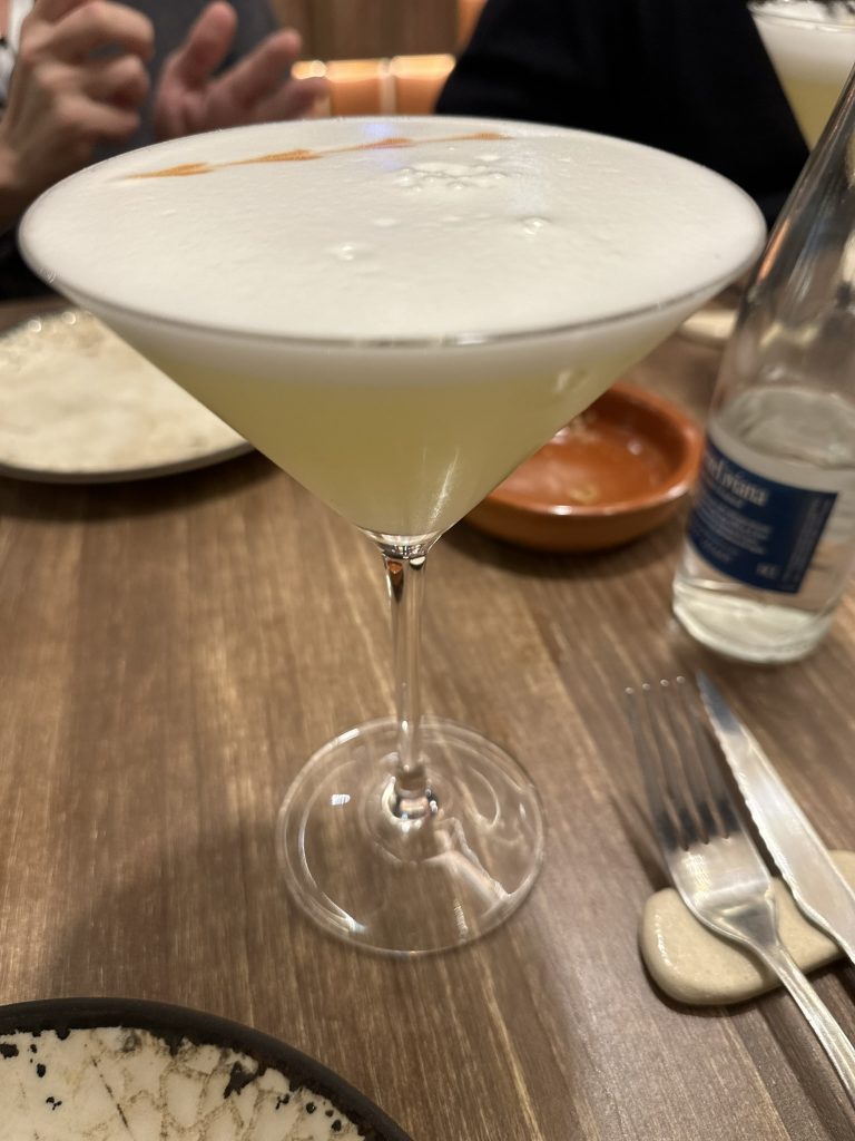 Un vaso de Pisco Sour clásico con su característica espuma blanca y unas gotas de amargo de Angostura en la parte superior.