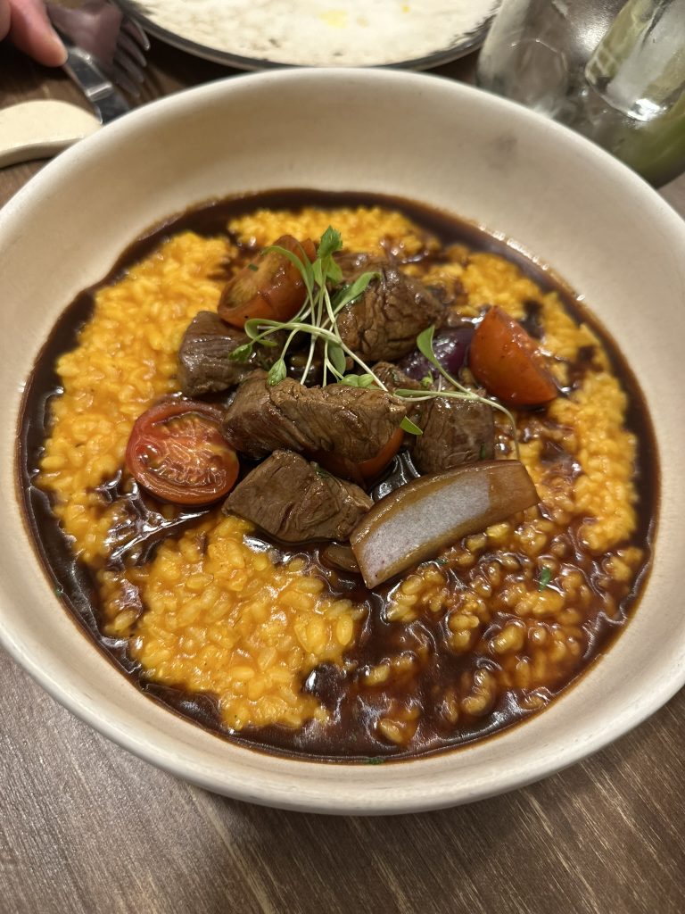 Un plato de arroz meloso de color amarillo intenso, con dados de solomillo salteados al wok y espolvoreado con cebolla china picada.