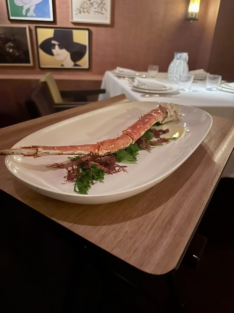 Patas y pinzas de cangrejo real del Mar de Barents partidas y presentadas en un plato blanco, acompañadas de mantequilla de hierbas y una rodaja de limón.