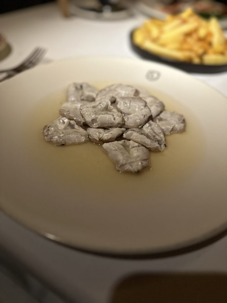 Kokotxas de merluza de Pasajes doradas a la brasa, servidas en un plato blanco con un toque de aceite y sal marina.