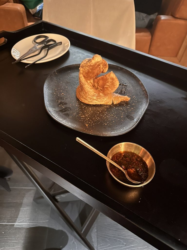 Oreja de cerdo frita, crujiente y dorada, servida entera y trinchada, acompañada de chimichurri verde y fresco