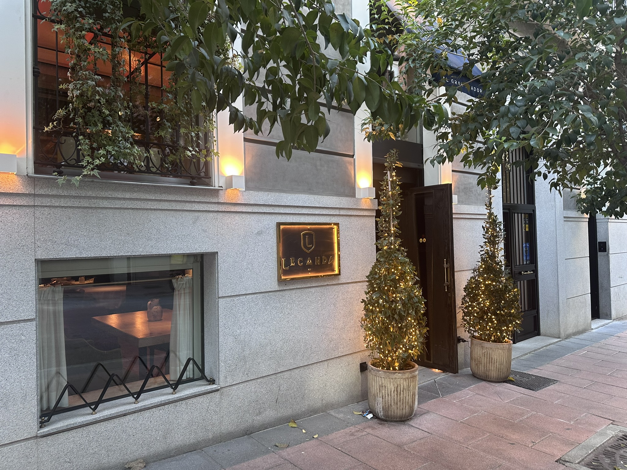 Fachada oscura de El Gran Asador Lecanda con letrero dorado iluminado, puerta de madera y farolillos a ambos lados.