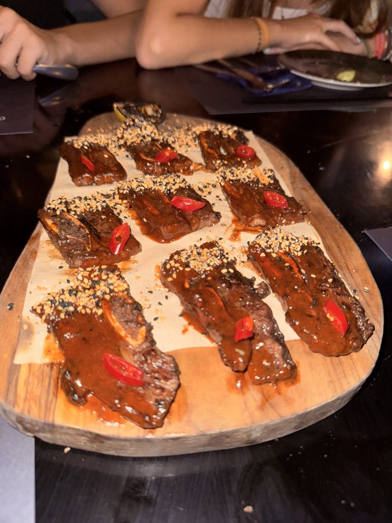 Costillar short rib de cerdo negro en El Cerdo Negro 1985, bañado en salsa BBQ y acompañado de guarnición, servido en plato rústico