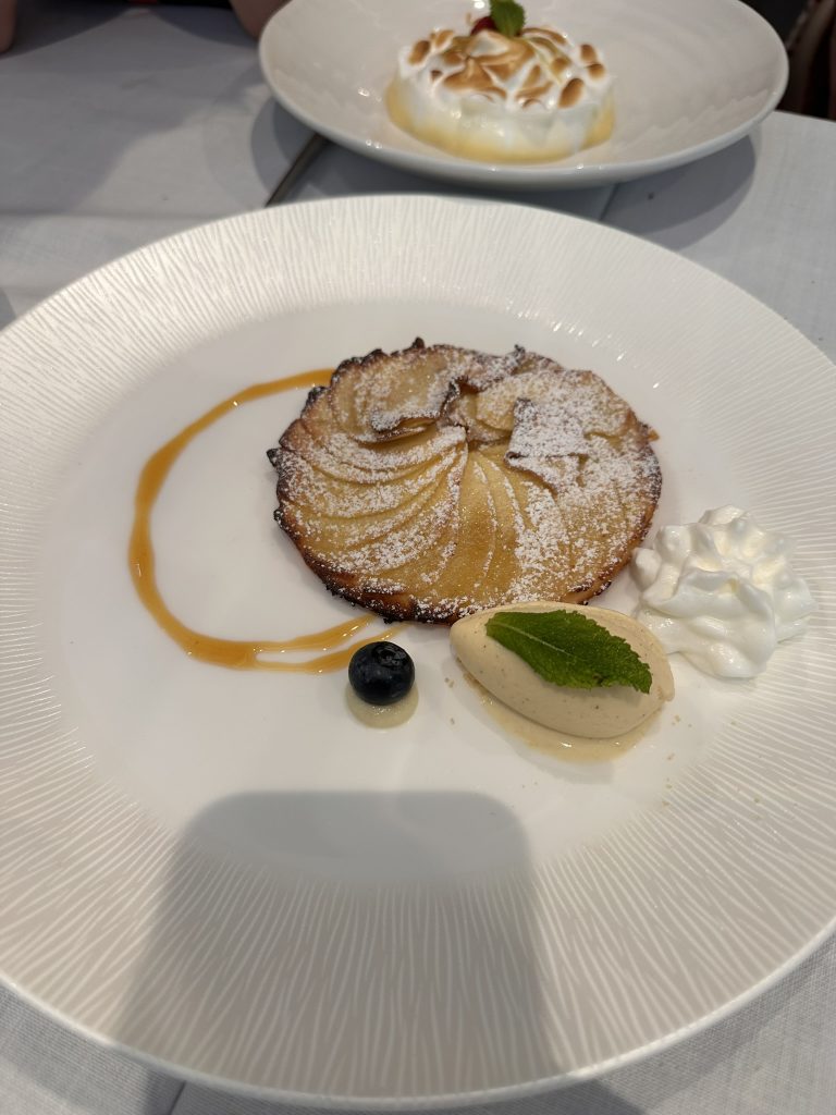 Porción de tarta fina de manzana con una base crujiente, láminas de manzana caramelizada y una bola de helado cremoso.