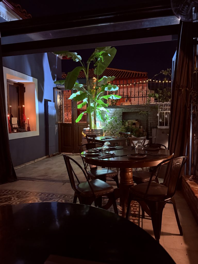 Terraza del restaurante El Cerdo Negro 1985 en Atenas, con mesas de madera, plantas alrededor y una iluminación tenue y acogedora