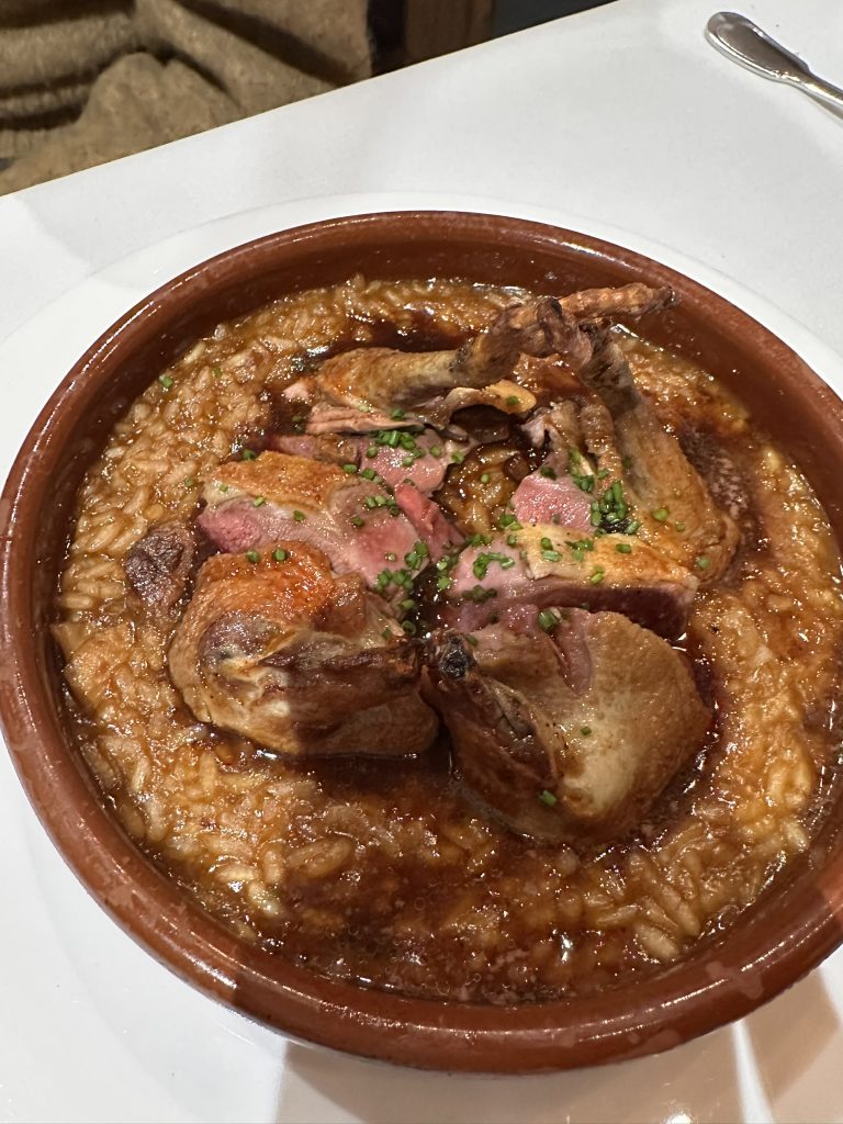 Primer plano de un plato de pichón asado con risotto de montaña, queso de Parma y salsa Perigourdine, una creación culinaria que te sorprenderá.